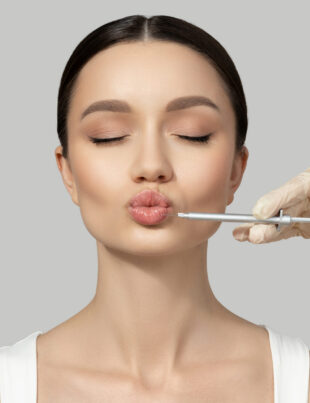 A beautiful girl makes an injection in the lips, on a gray backg